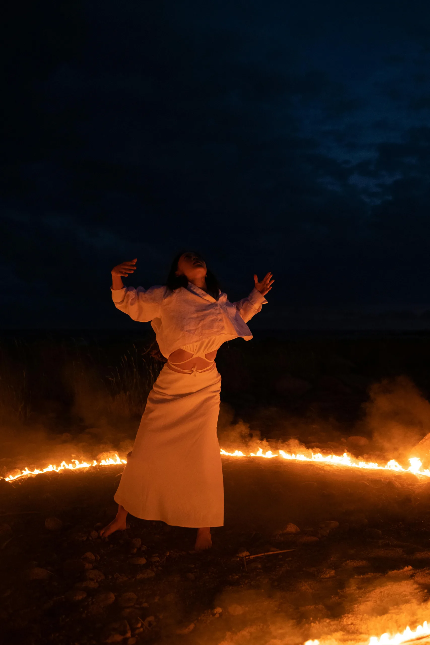 Black magic A woman performs an enchanting ritual within a ring of fire under a dark night sky, evoking mystical allure.