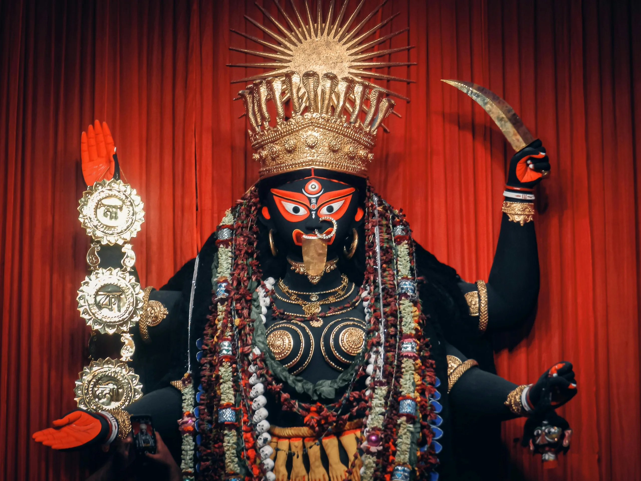 A prominent statue of Hindu goddess Kali adorned with intricate details and red backdrop, showcasing spirituality.