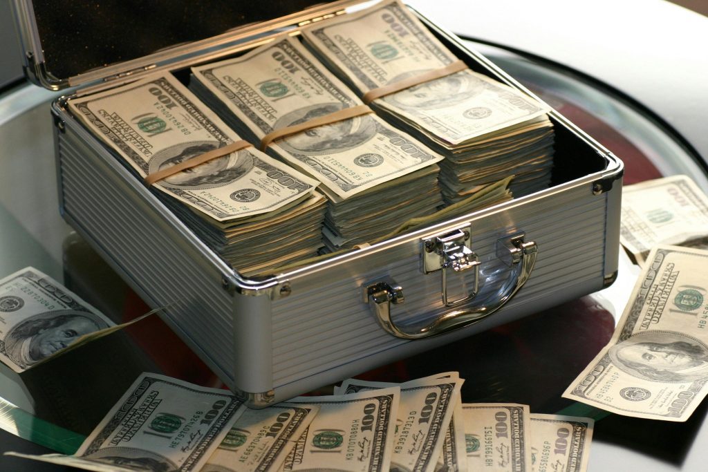 Cash Billionaire cash. Open briefcase filled with stacks of hundred dollar bills on a glass table, representing wealth.