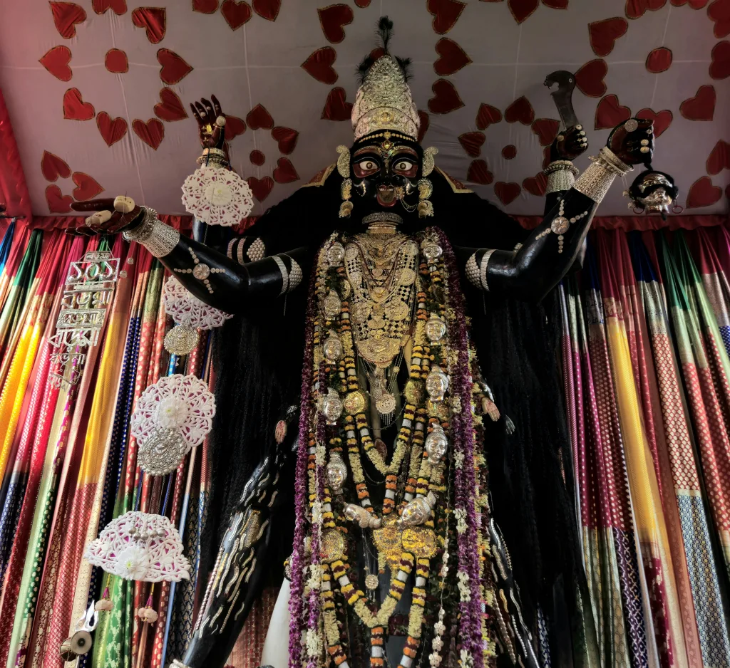 kalika Intricate statue of Goddess Kalika adorned in traditional ornaments, surrounded by vibrant drapes in a temple setting.