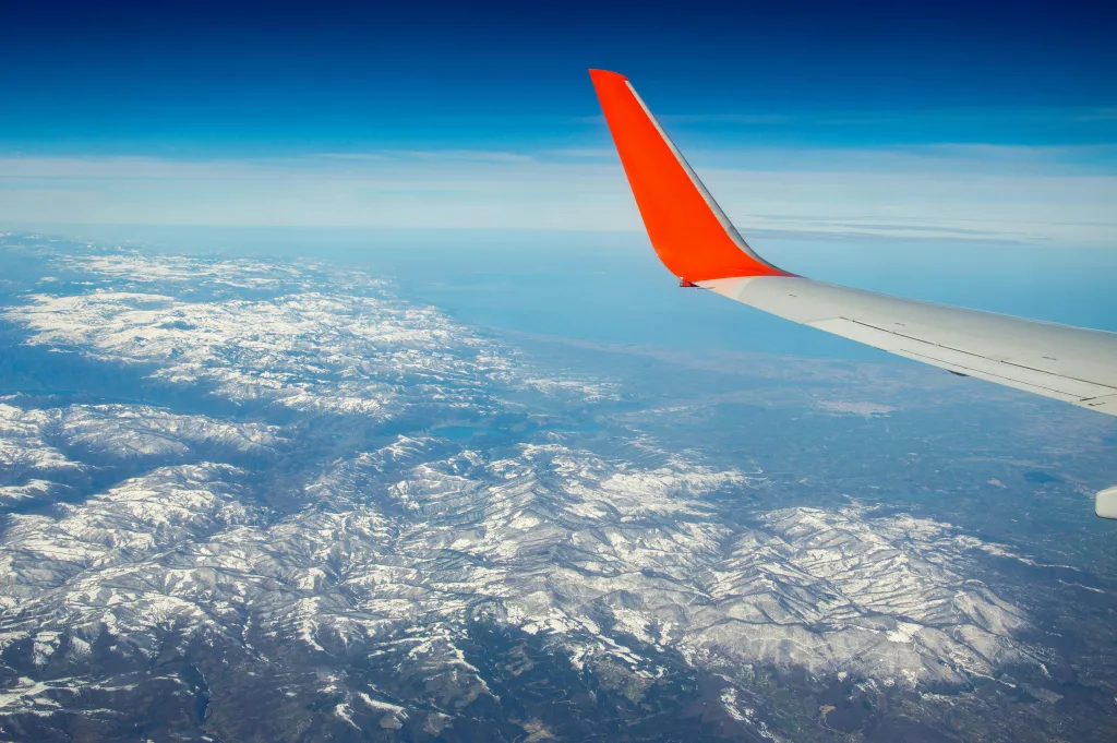pexels-photo-31181797-31181797 Scenic aerial view of snow-capped mountains from a plane, featuring a vibrant red wing.