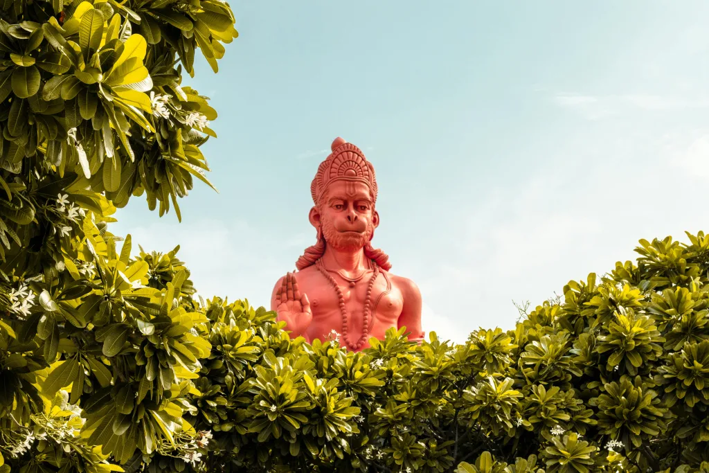 Hanumanji A vibrant red statue of Hanuman surrounded by green foliage under a clear sky. this image represent bajrang baan text of hanumani
