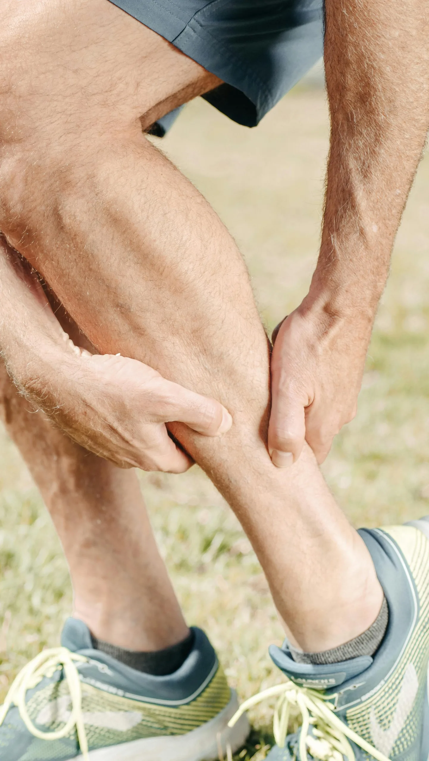 A man outdoors massaging his calf, dealing with muscle pain during sports activities. the pain is caused due to nightly leg cramps