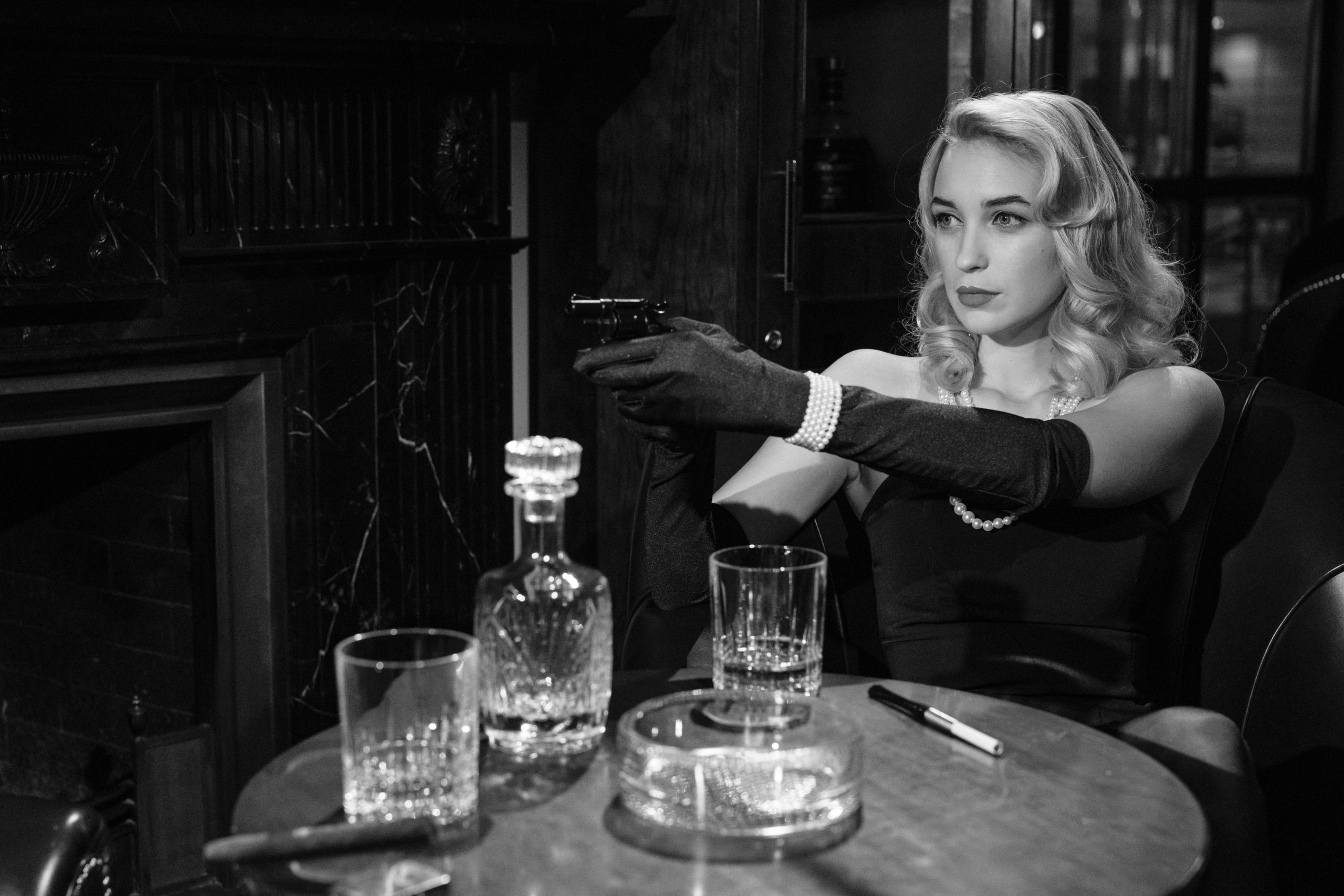 Elegant femme fatale holding a handgun, creating a vintage noir atmosphere indoors.