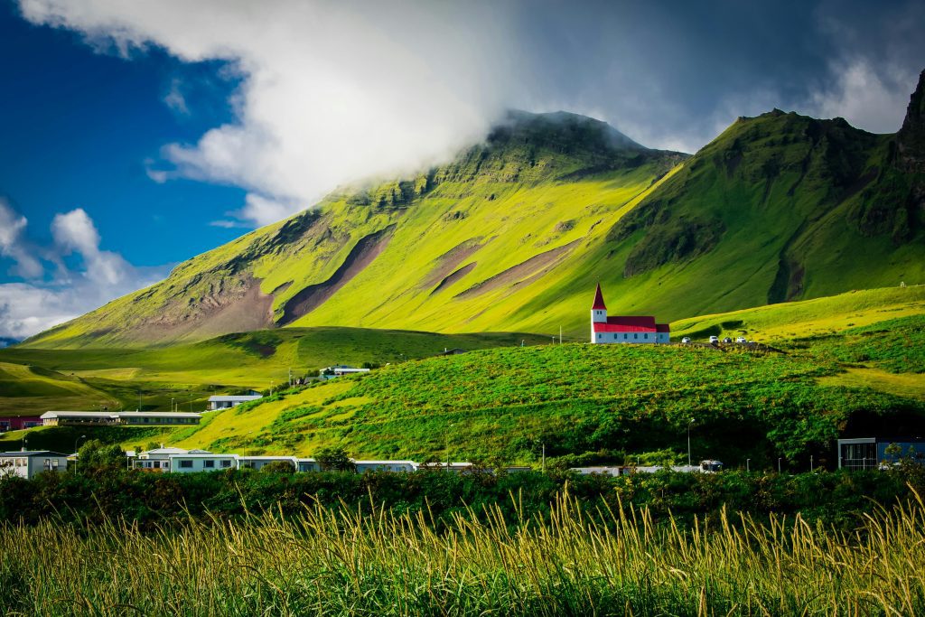 Iceland Beautiful landscape of a red-roofed church nestled in lush green hills under a vibrant sky in Iceland.