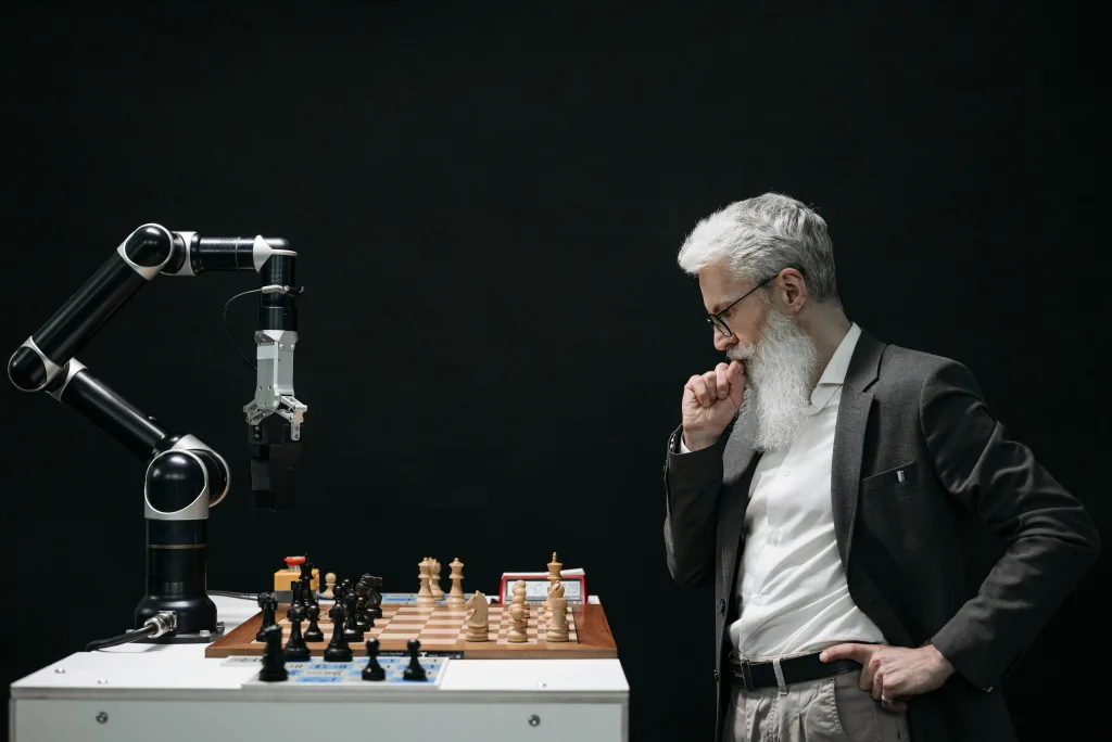 pexels-photo-8438918-8438918 An elderly scientist contemplates a chess move against a robotic arm on a chessboard. where it is being teated ai for smes